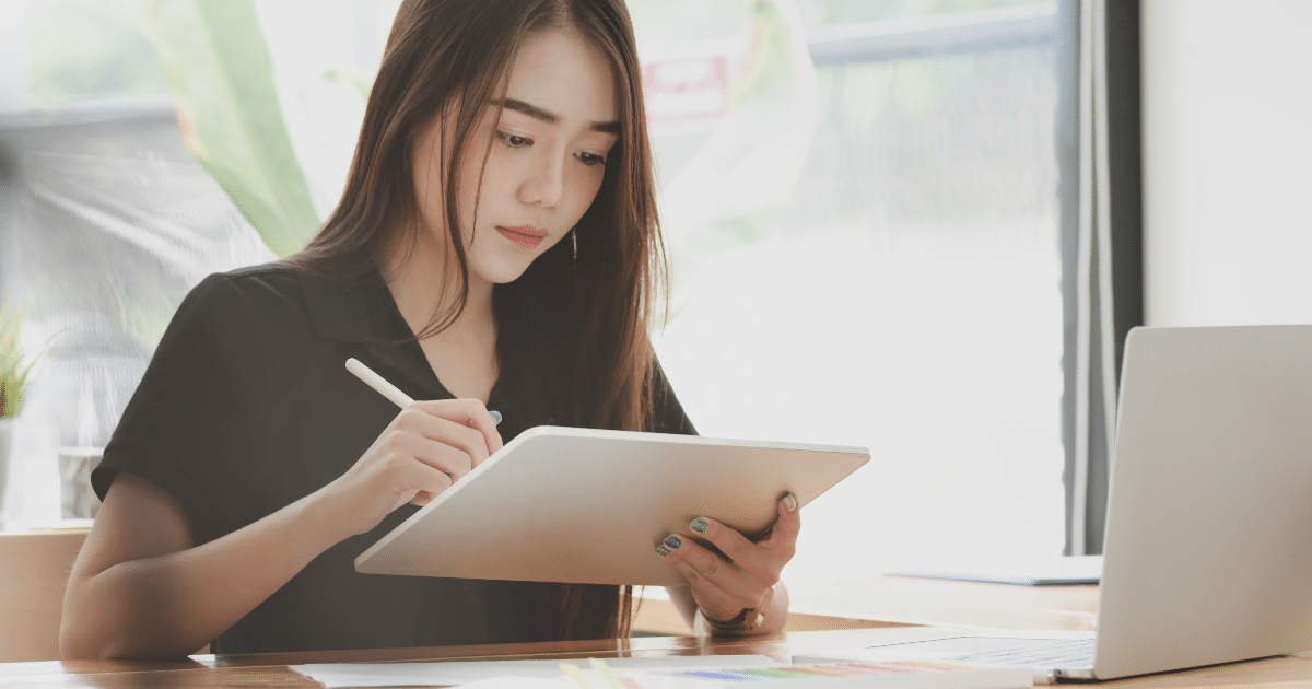 female sitting at desk working on tablet with pen